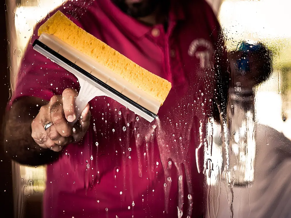 Window cleaner pulling a squeegee across a wet pane of glass